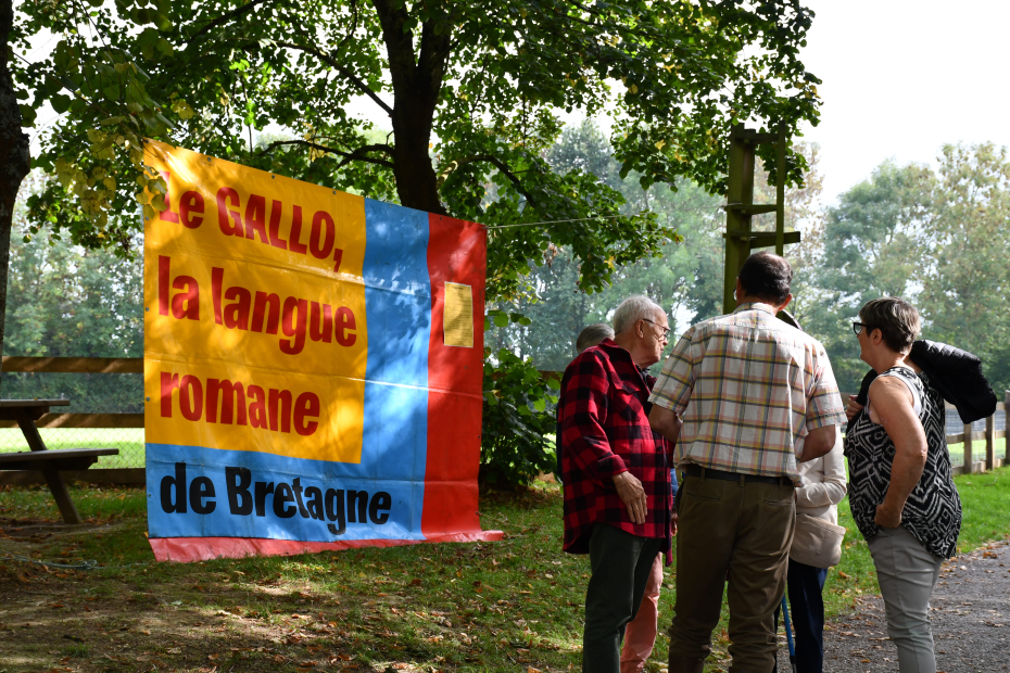 Un groupe discute en gallo devant une grande bâche portant la mention 